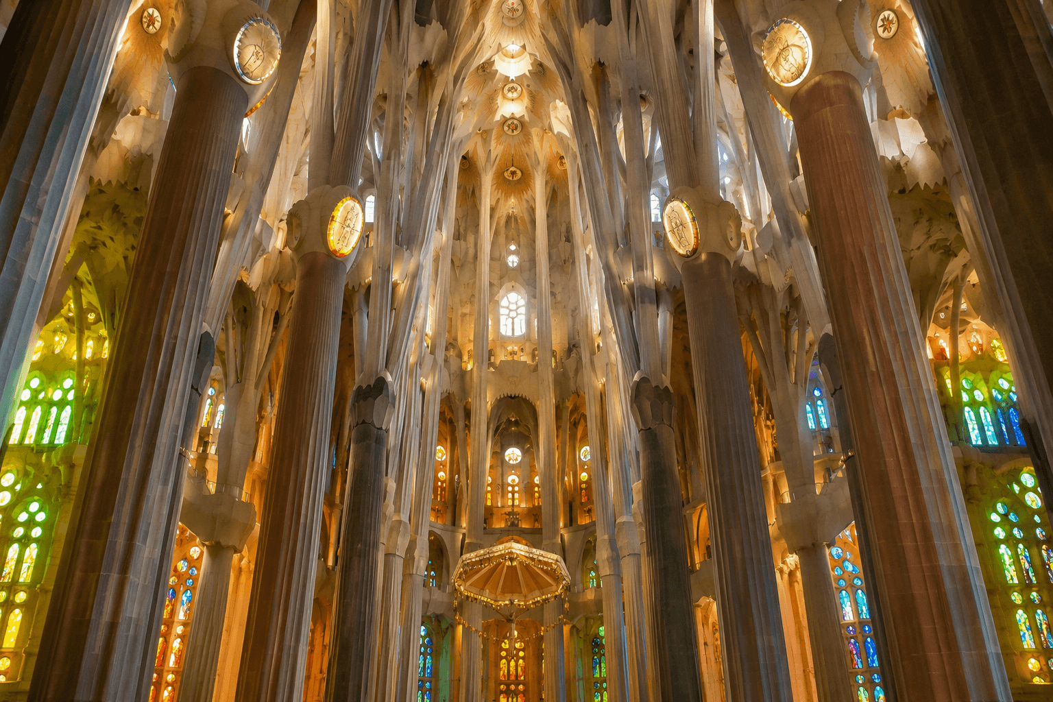 Interior of Sagrada Familia in Barcelona with tree-like columns, vaulted ceiling and colourful stained-glass windows.